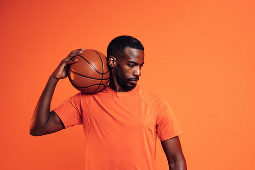 Male athlete standing in the studio with basket ball on his shoulder looking down