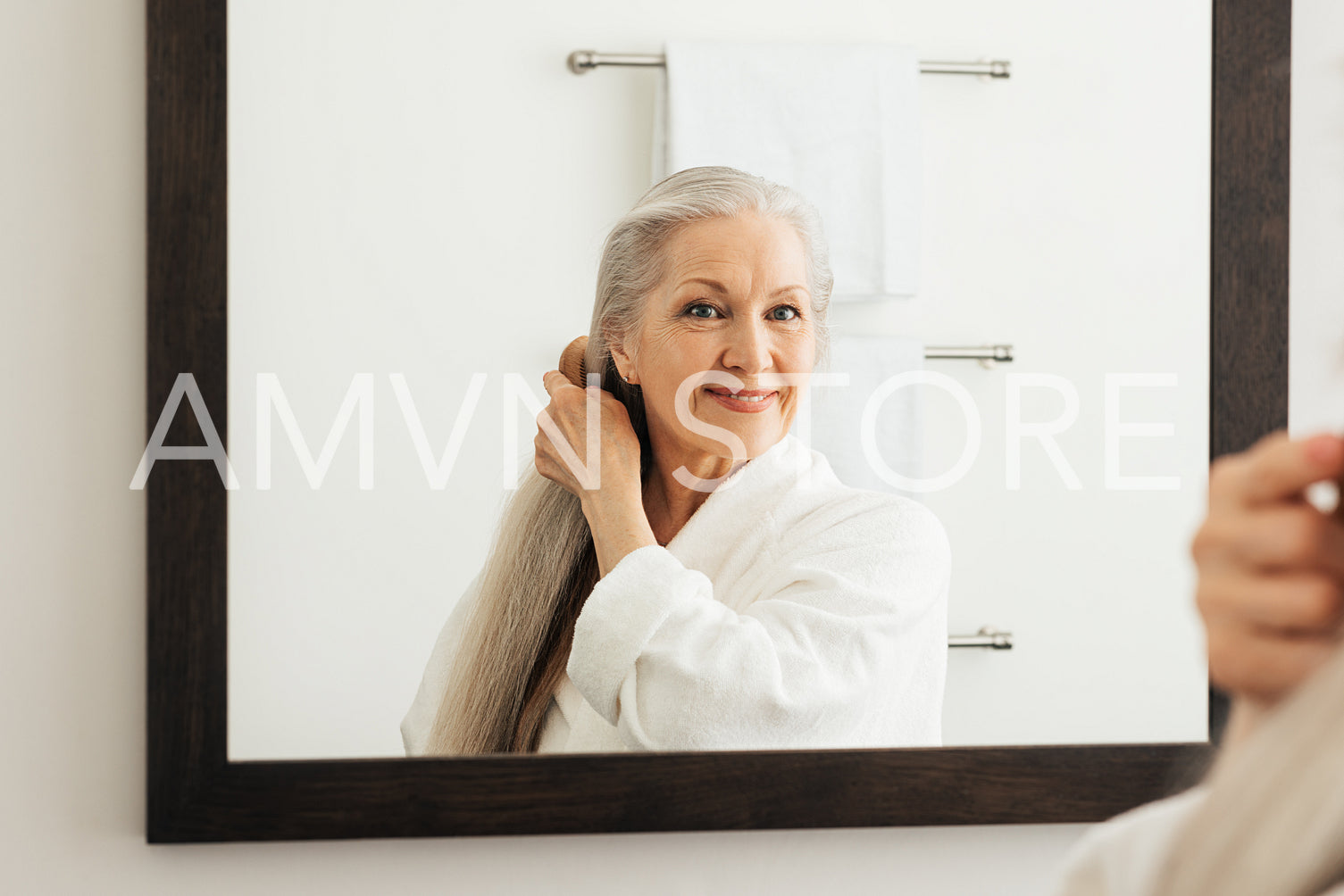 Portrait of a senior woman with a wood comb looking at a mirror. Aged female combing her beautiful long grey hair.