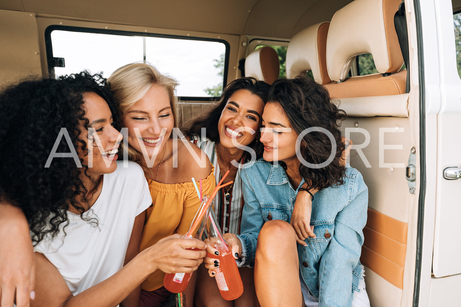 Two smiling women toasting with bottles in van. Close friends enjoying summer road trip.