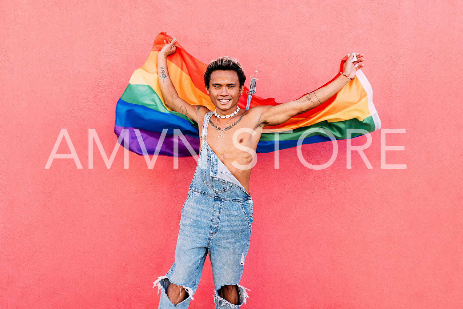 Happy guy waving rainbow lgbt flag against pink wall outdoors