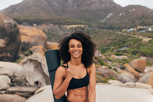 Portrait of a smiling fit woman with closed eyes holding a mat while standing by mountains in valley