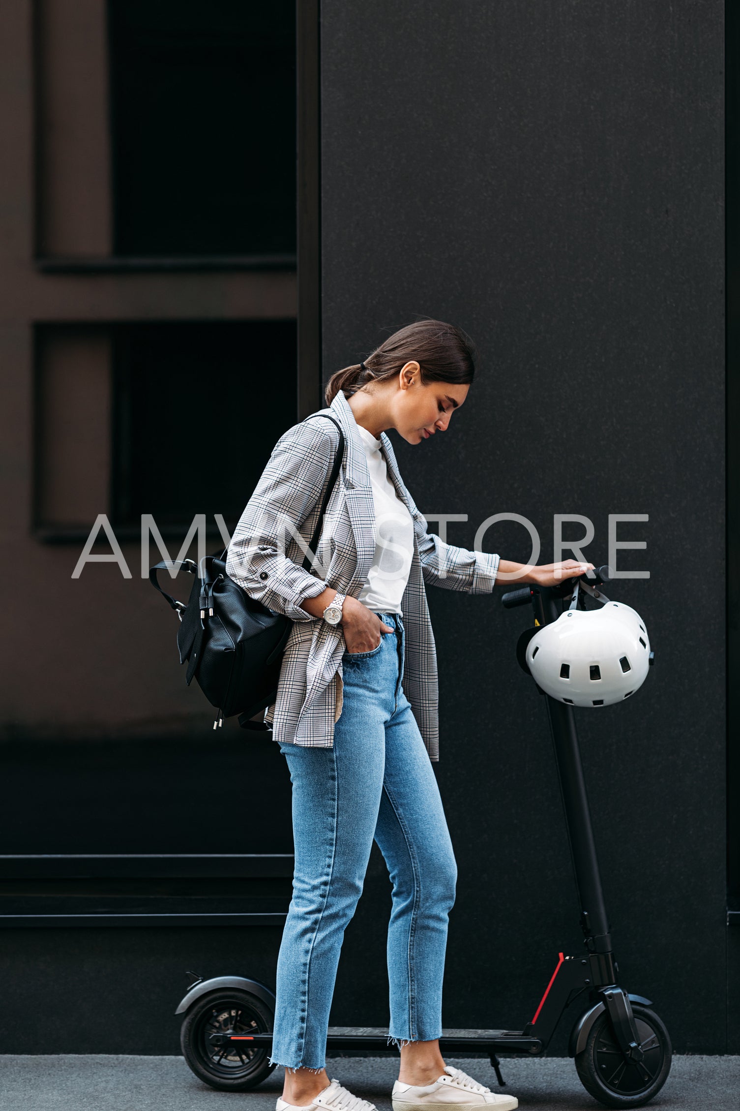  Full length shot of young businesswoman standing at a building with electric push scooter looking down