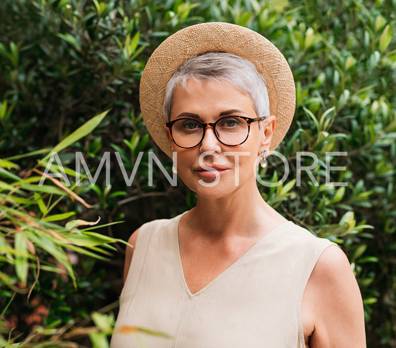 Senior woman with short grey hair, glasses, and straw hat looking at camera in a park