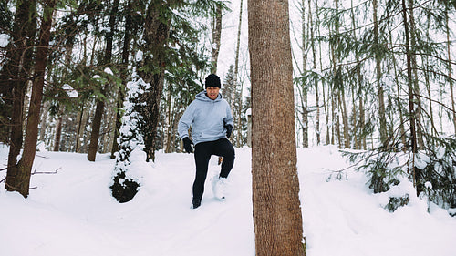 Young man exercising in the forest, running down through a snow