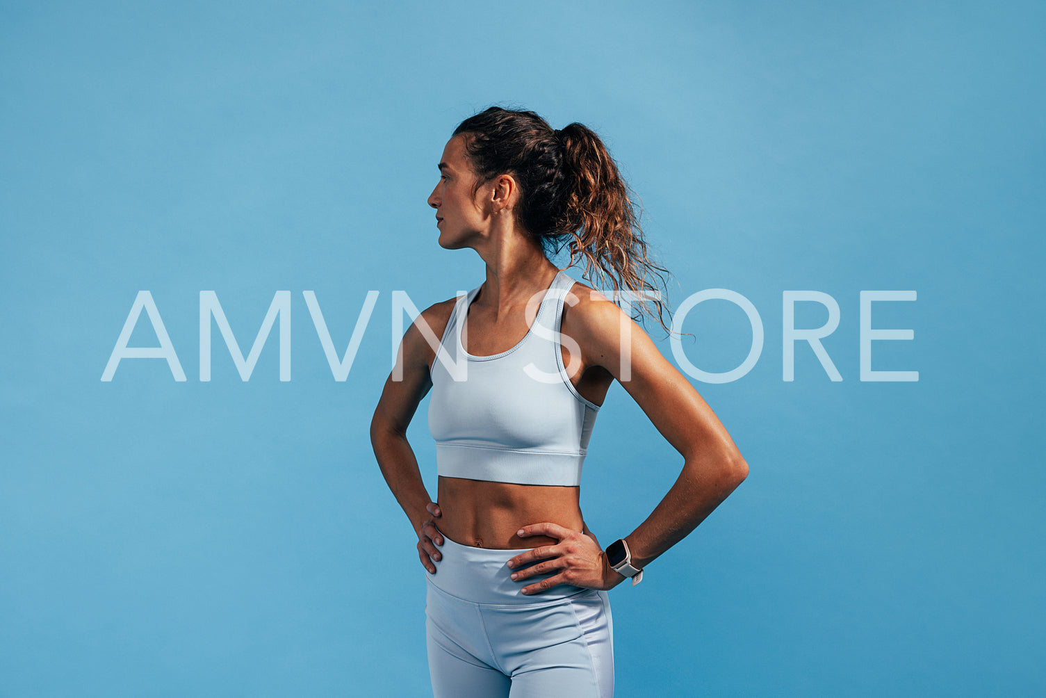 Side view of fitness female with hands on her waist standing on blue background