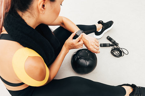 High angle of female athlete checking pulse on smart watch after exercises indoors