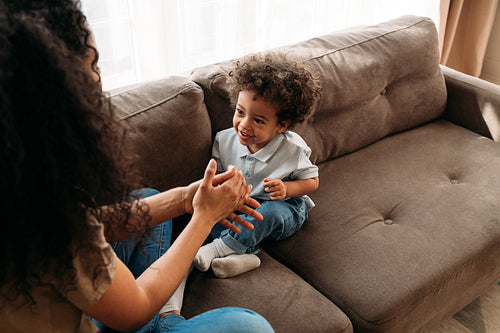 Son and mother sitting on a sofa in living room and playing