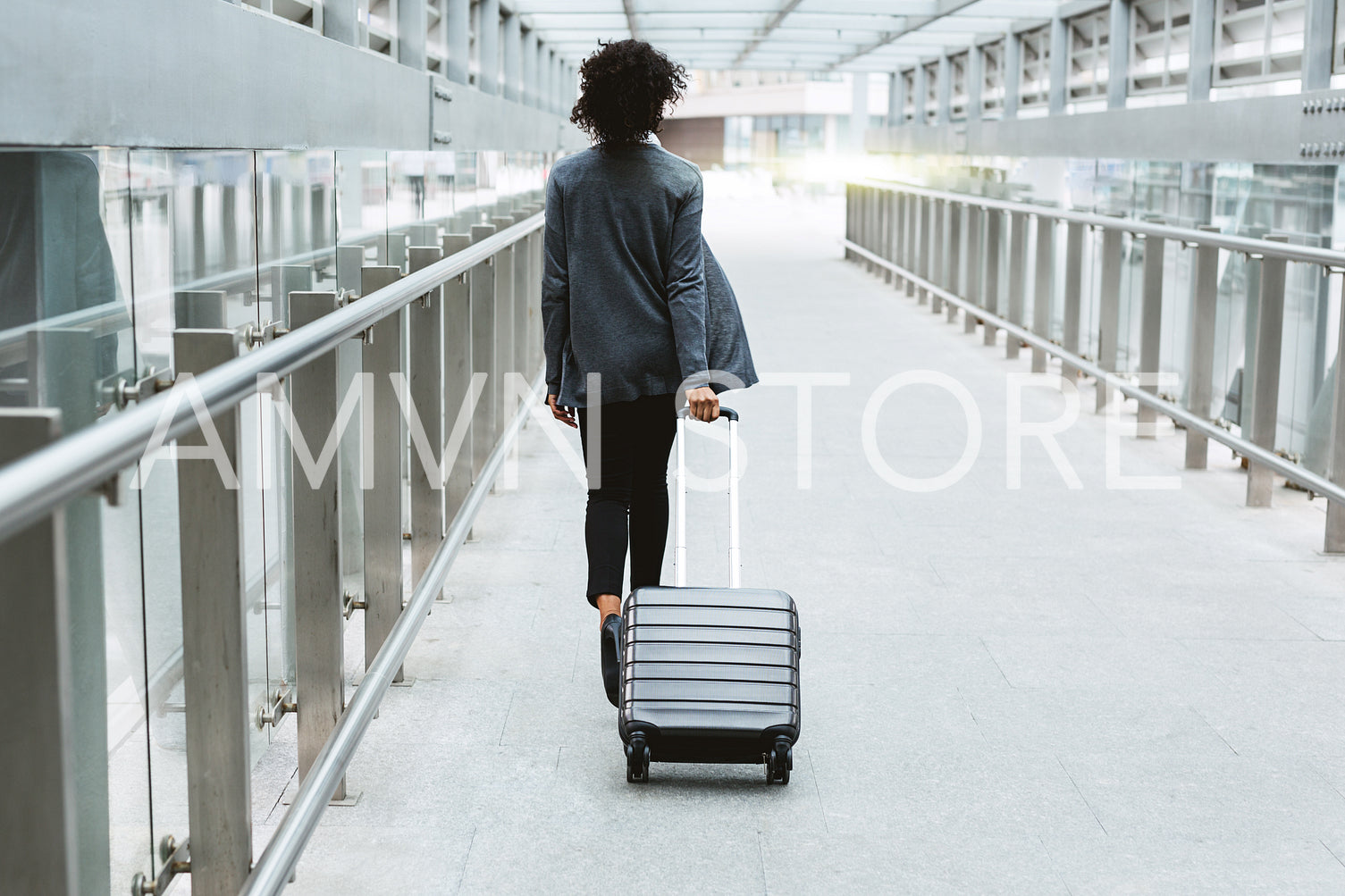 Back view of businesswoman walking with suitcase in airport corridor	