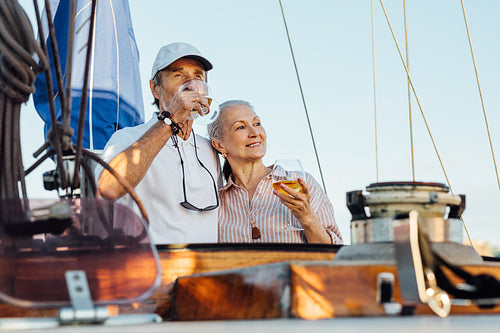 Portrait of senior couple standing on a private sailboat and drinking wine. Woman and man with bocals of wine on yacht enjoying trip.