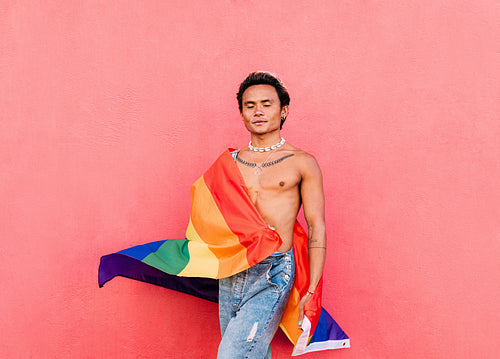 Handsome guy with rainbow lgbt flag standing against pink wall outdoors