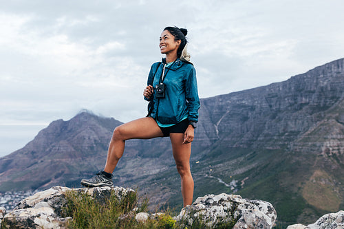 Young woman with backpack standing on the top of a hill. Smiling female enjoying being on the top of the mountain.