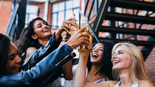 Group of female friends toasting with beer bottles outdoors