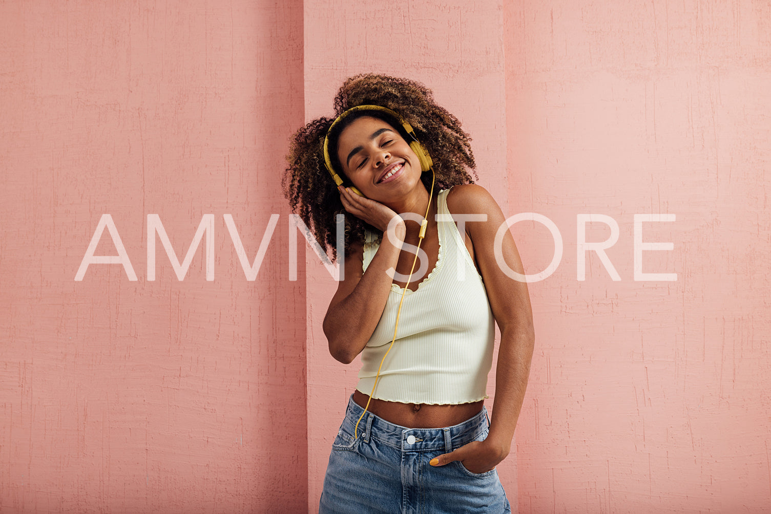 Woman with curly hair relaxing at pink wall listening to music w