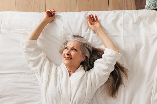 Pleased senior woman lying on a bed wearing bathrobe