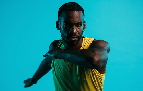 Close up of serious and sweated athlete doing stretching exercises in the studio over blue background