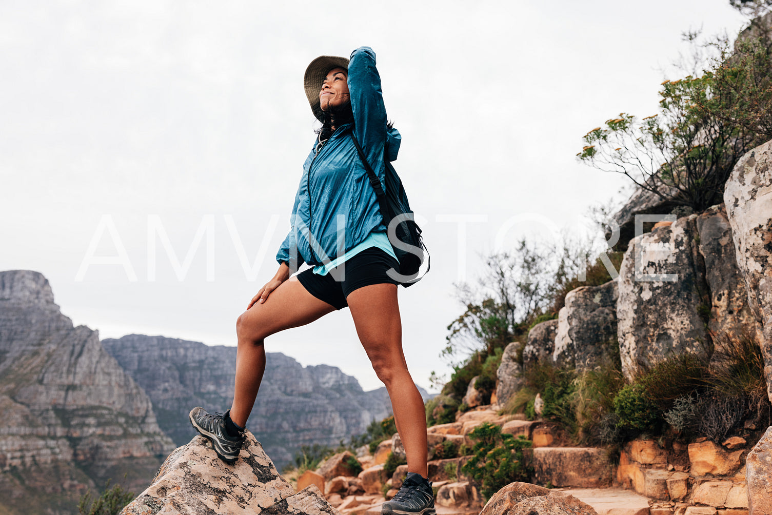 Smiling woman hiker in sports clothes holding a hat on her head while looking up and enjoying the view