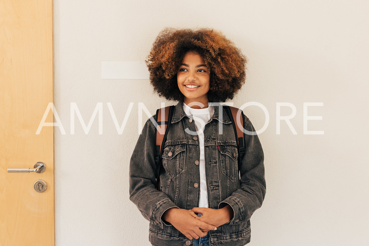 Beautiful girl with curly hair wearing backpack standing at wall in college