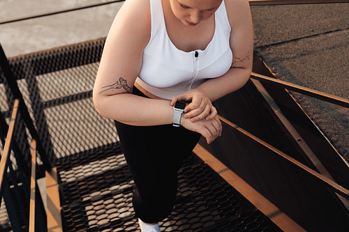 Unrecognizable curvy woman checking activity tracker while stepping up on staircase outdoors