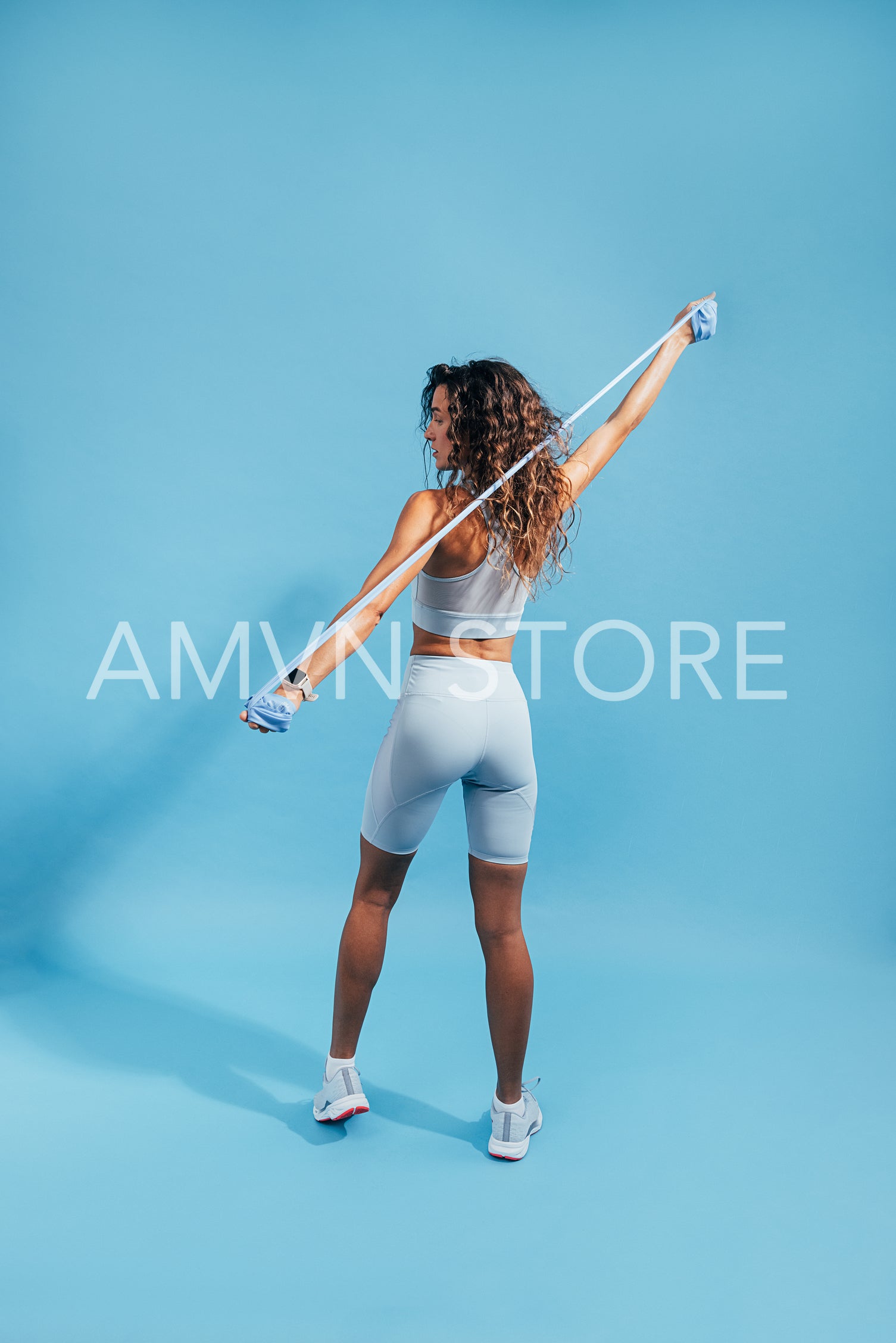 Rear view of fit young woman stretching arms with rubber band on blue background