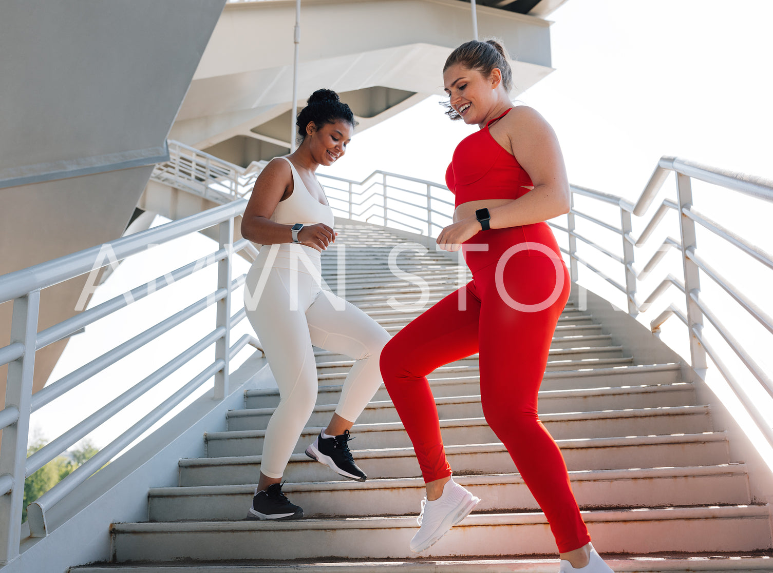 Two young plus-size females running together downstairs while practicing outdoors. Smiling women doing workouts together.