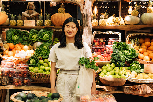 Smiling woman with a shopping bag at an outdoor market. Asian woman looking at camera while standing on a street market.