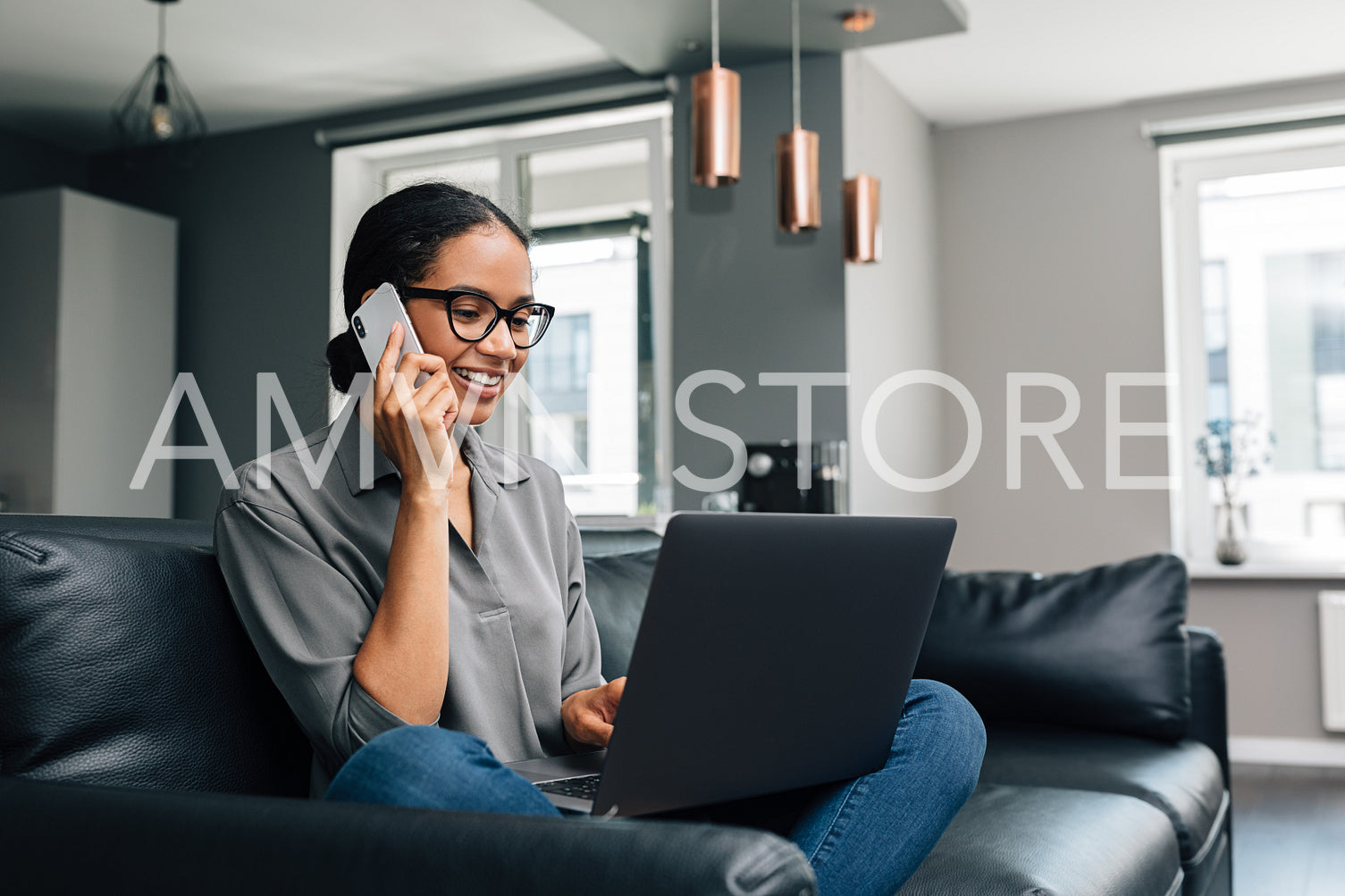 Smiling woman sitting on a sofa with laptop on her legs and making a phone call	