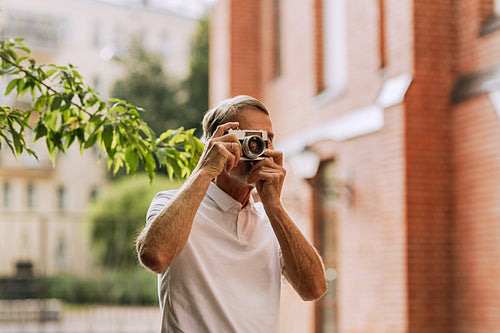 Senior tourist walking in the city and making photographs on a film camera