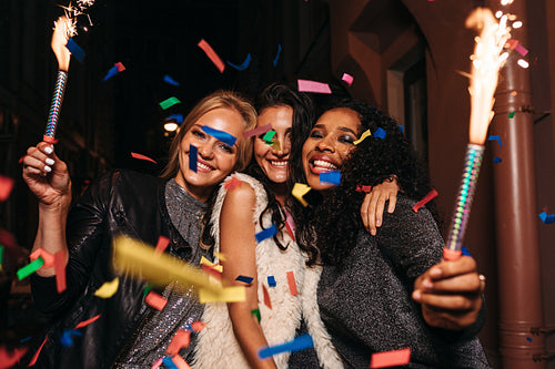 Friends having fun with confetti and sparklers at night city