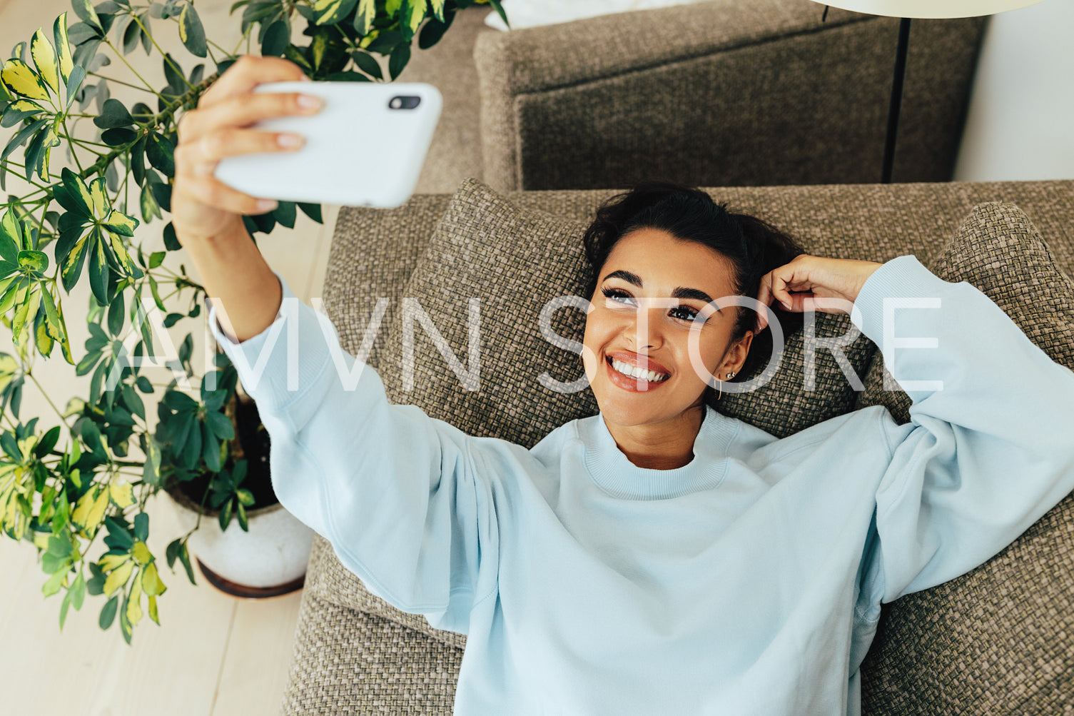 Beautiful happy woman lying on a sofa in a living room a taking selfie. Woman making photographs for social media indoors.	