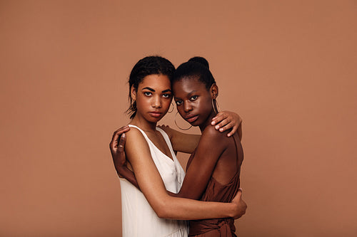 Two diverse women friends against brown background embracing each other