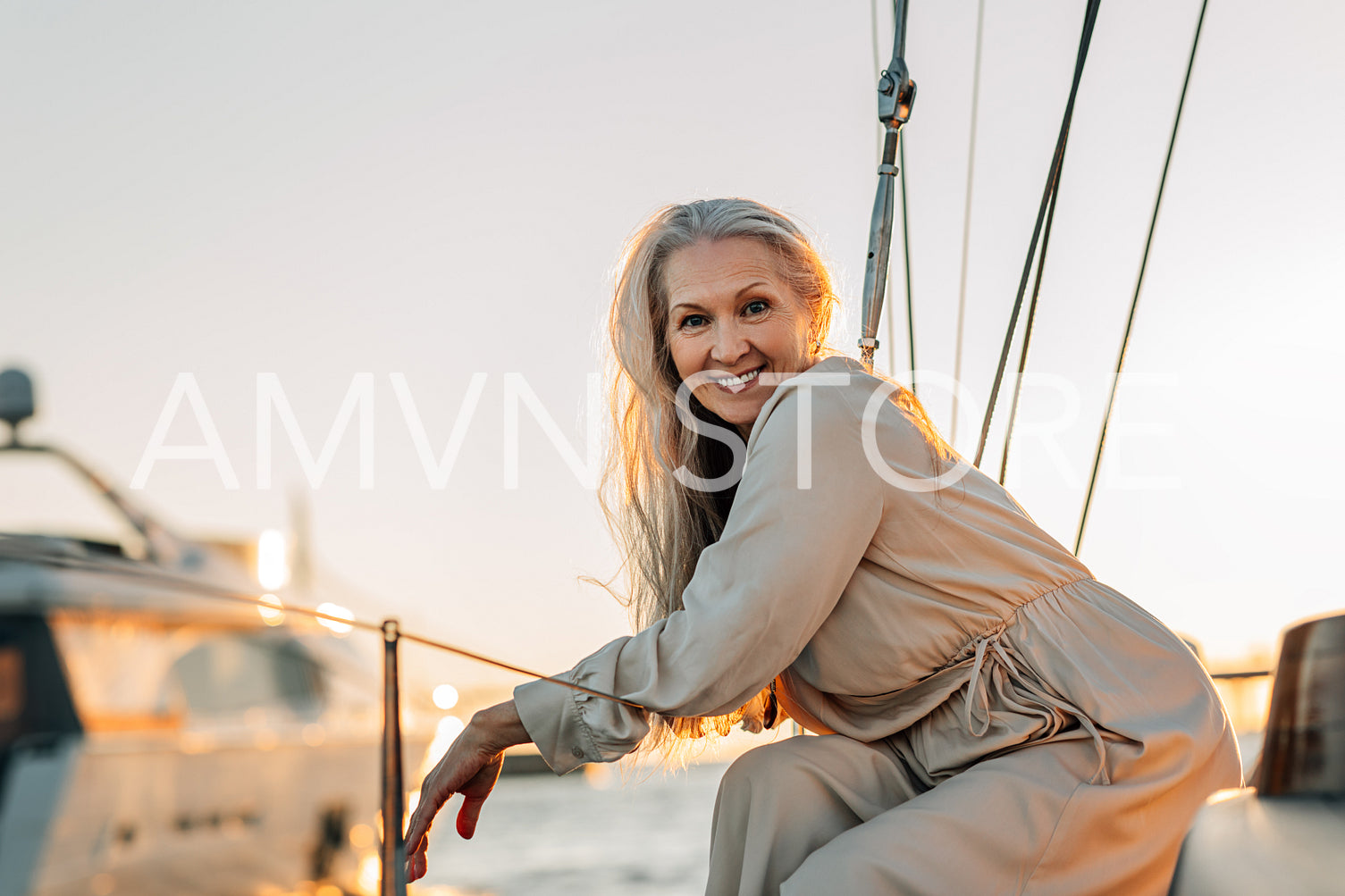 Cheerful mature woman sitting on yacht deck and looking at camera. Happy senior female enjoying weekends water trip.