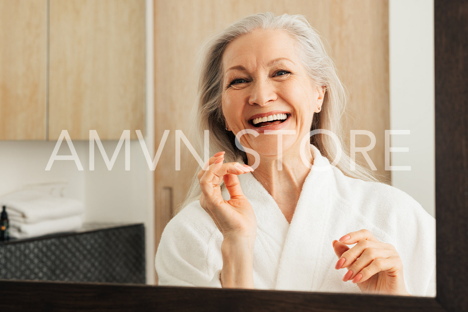 Happy mature woman with grey hair in the bathroom. Smiling female in a bathrobe.