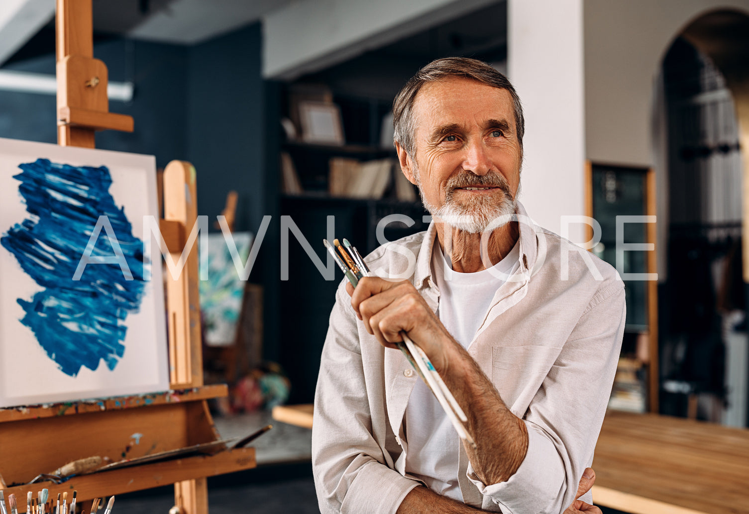 Portrait of a smiling mature painter sitting in his studio and looking away	