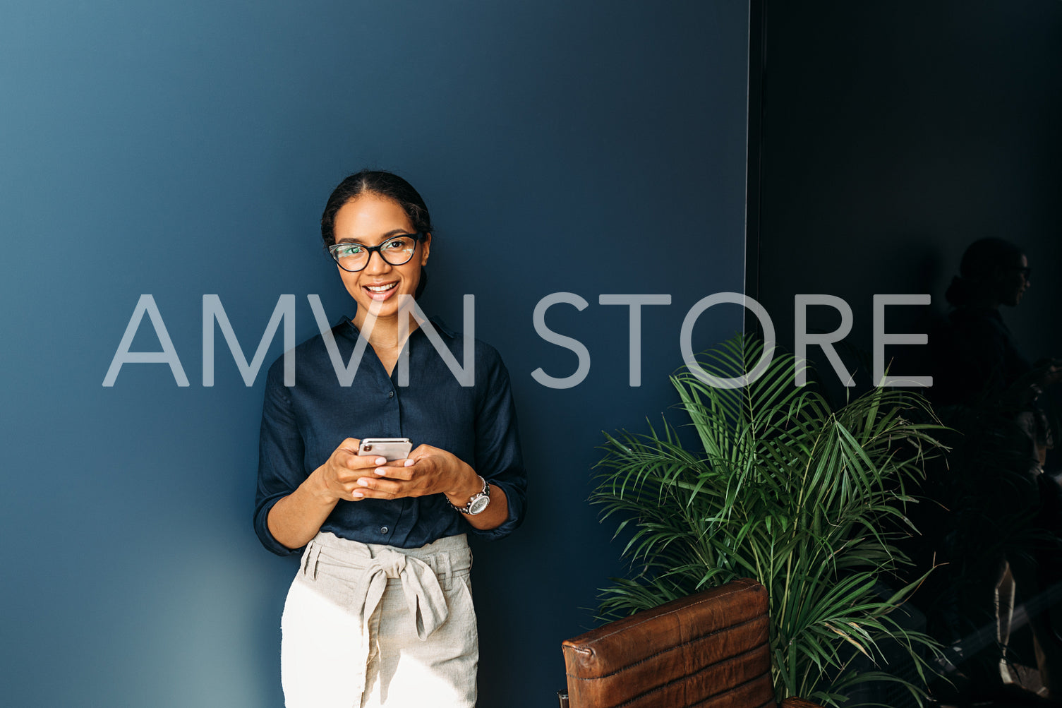 Beautiful smiling woman looking at camera while using a smartphone at a home office	