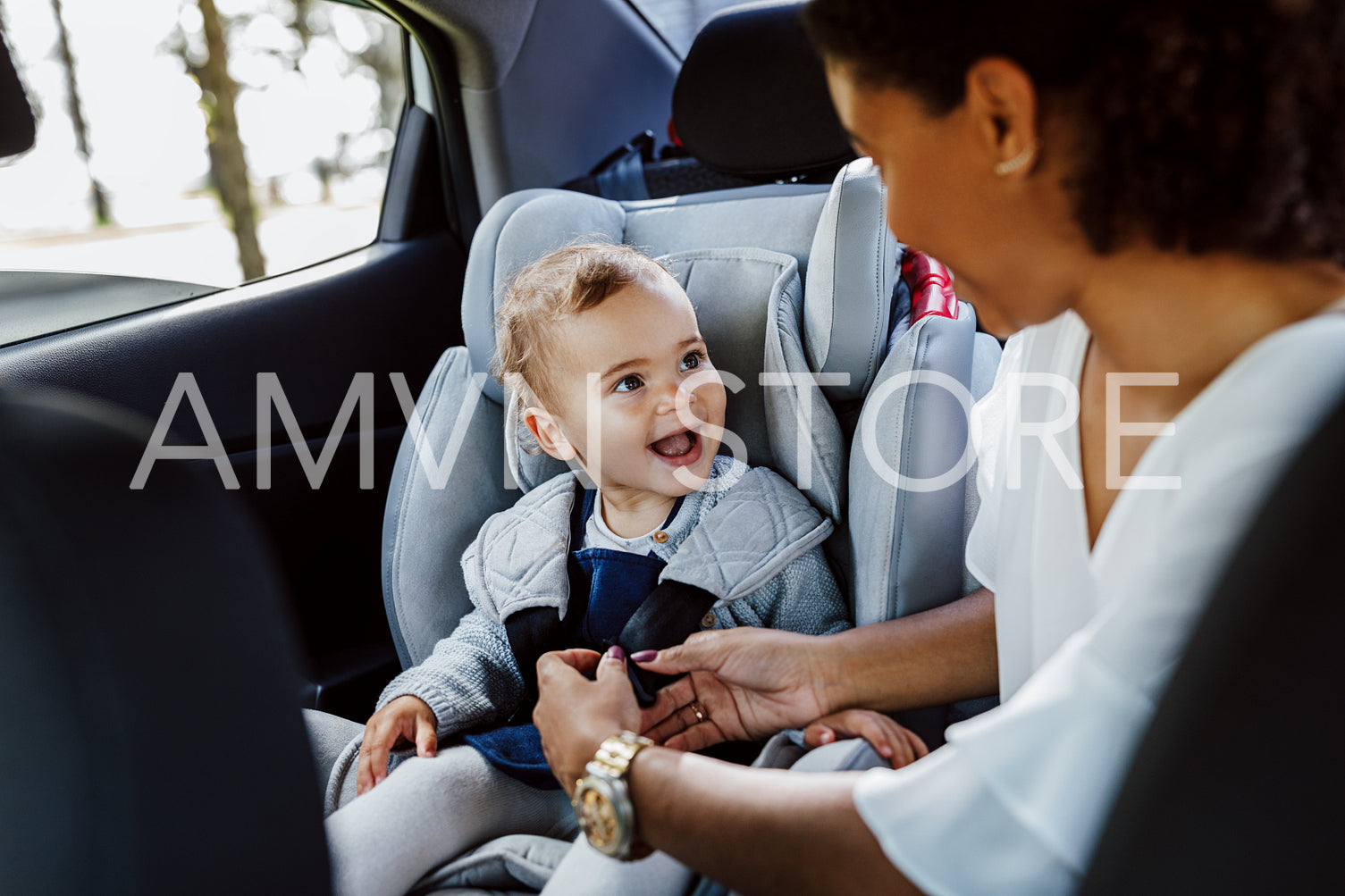 Happy baby girl looking at her mother in a car. Woman fastening safety belts while daughter looking on her.	