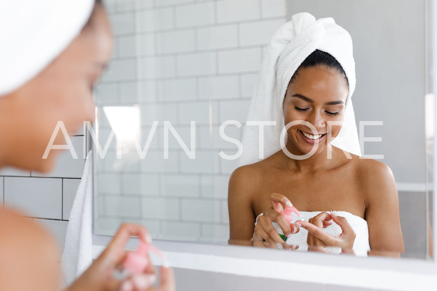 Happy young woman applying face cream in bathroom, standing in front of a mirror	