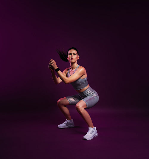 Full length of a slim female in silver sportswear doing sit-ups over a magenta background