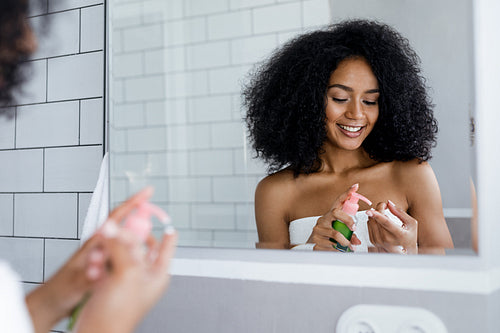 Smiling woman prepare for applying cosmetic cream on face in bathroom, standing in front of a mirror