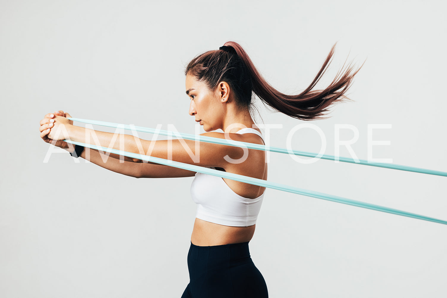 Side view of sportswoman exercising with resistance band against white wall