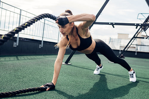 Fitness woman exercising with battle rope outdoors. Muscular athlete working out on a terrace.