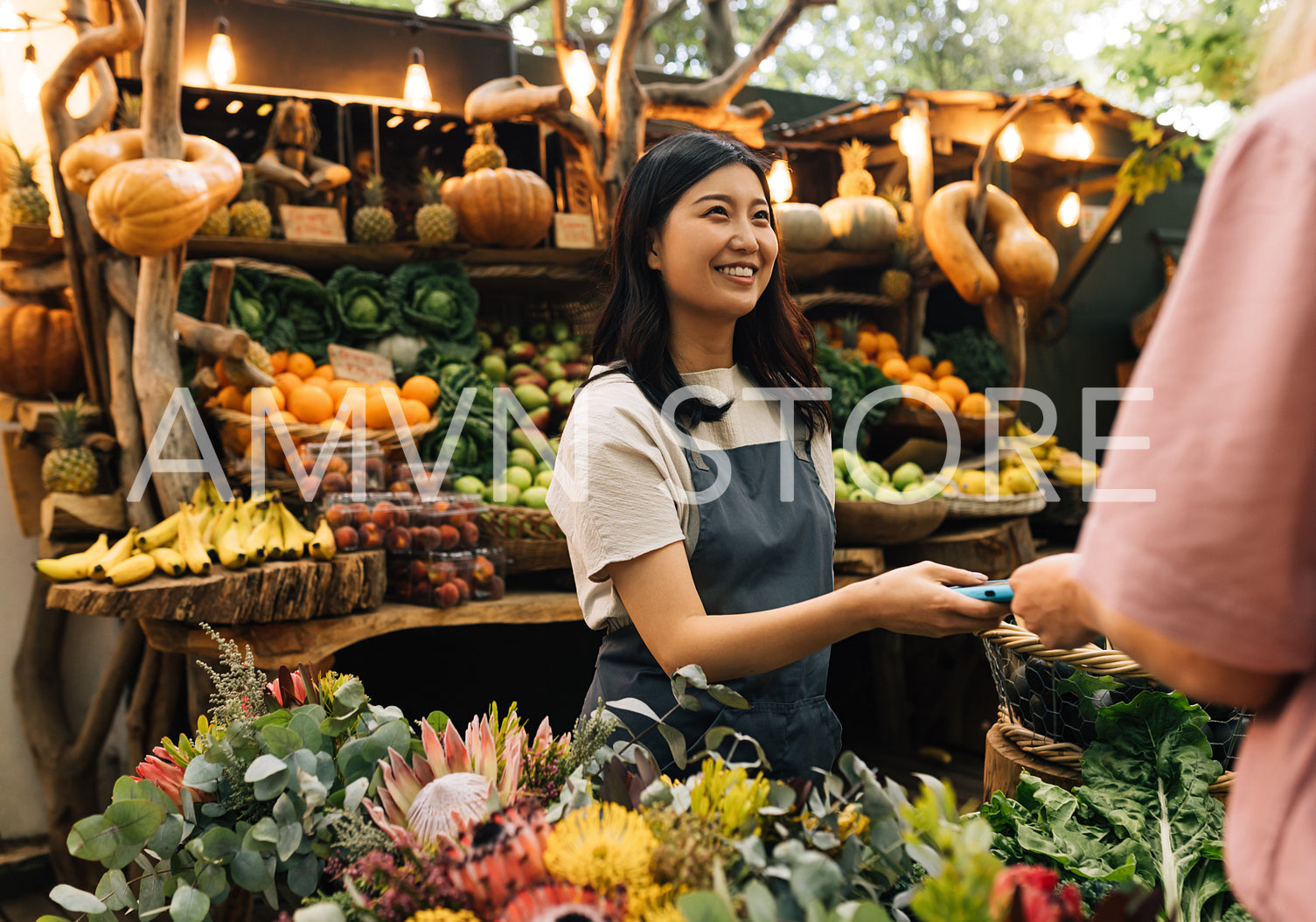 Vendor receiving payment on the outdoor market. Woman in an apron working at a farmers market looking at customer.