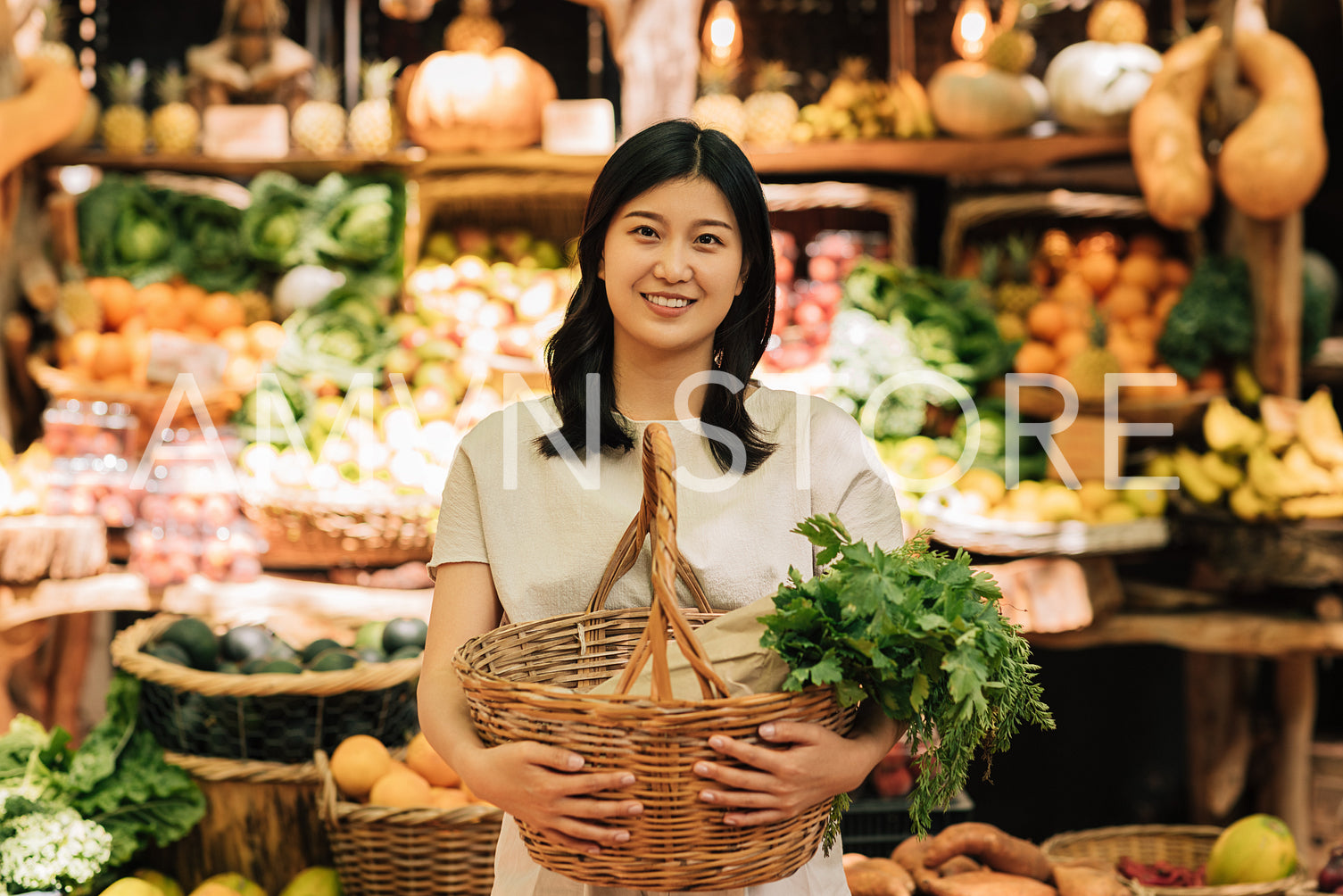 Smiling Asian woman holding a wicker basket with vegetables. Young female standing outdoors on the farmers market.