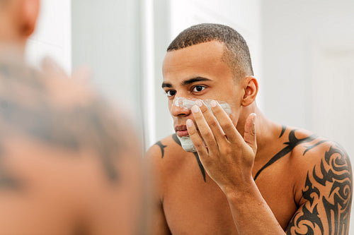 Young man applying anti-aging cream on his face