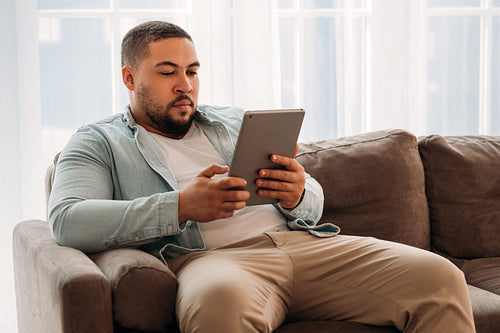 Young man using digital tablet surfing the internet on the couch