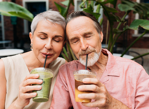 Mature couple drinking a smoothie. Wife and husband drink cocktails while sitting head to head with closed eyes.