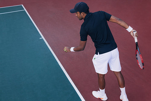 Young professional tennis player preparing to serve ball in a game, standing at baseline