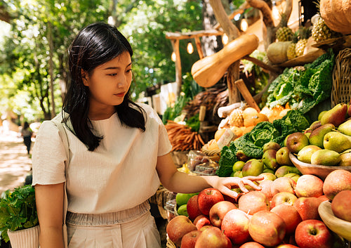 Woman choosing apples at a farmers market. Young female customer on street market looking for healthy food.