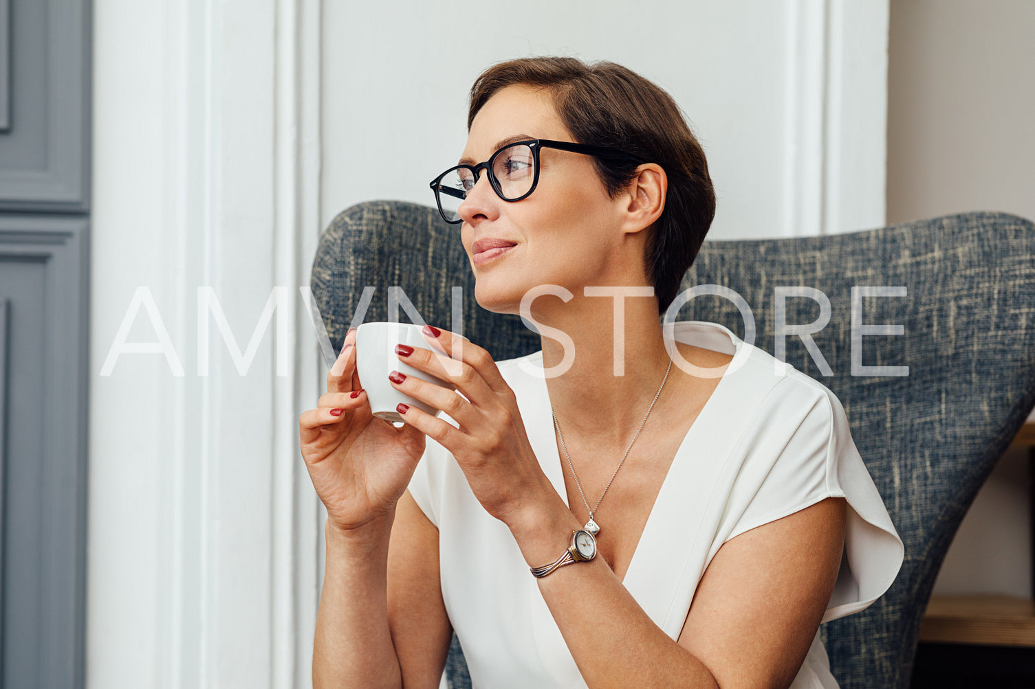 Businesswoman sitting on armchair in her apartment and holding a cup of coffee	