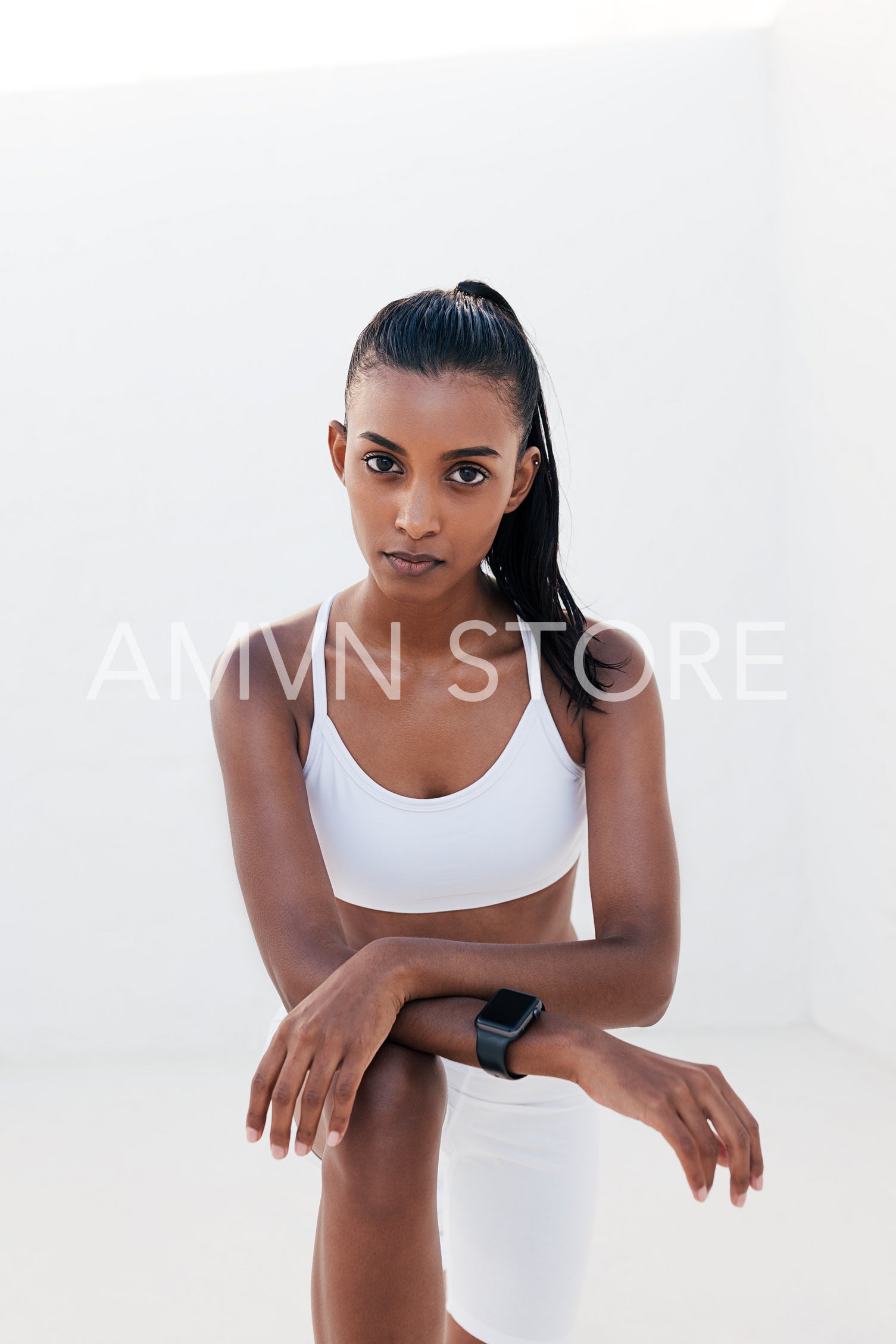 Confident woman in white sports clothes relaxing outdoors. Slim female leaning on her knee taking a break.