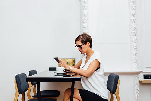 Woman sitting at table in luxury apartment and reading from digital tablet